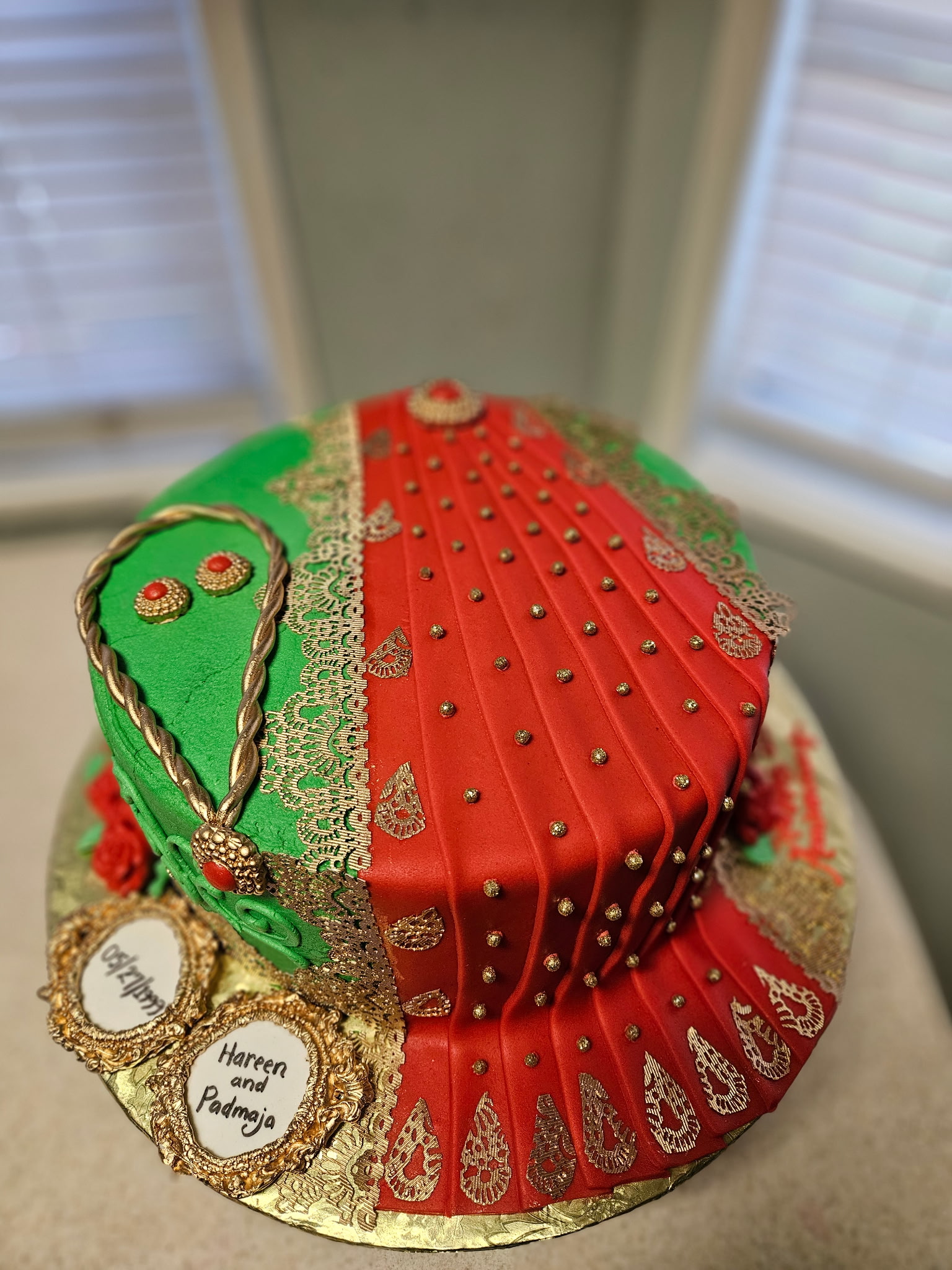 Sari-themed Indian wedding cake hand-piped in deep red and green with intricate gold-lace beadwork and name medallions.