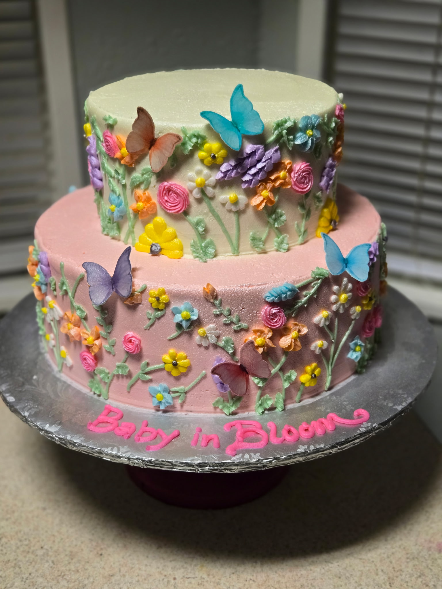 Two-tier Baby in Bloom shower cake with hand-piped wildflowers in pink and pastel and butterfly accents.
