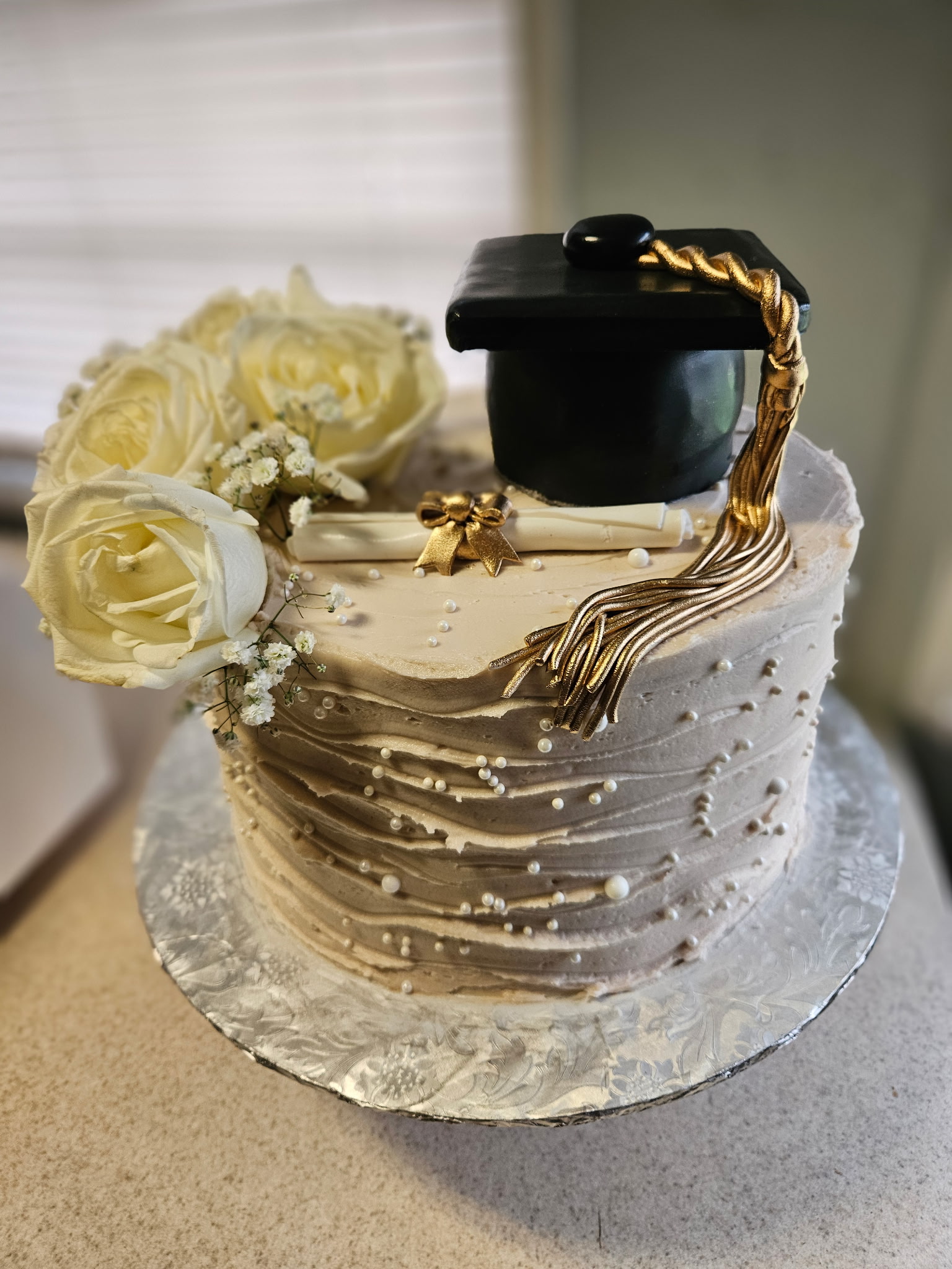 A cream textured-buttercream graduation cake with fresh white roses and a graduation-cap topper