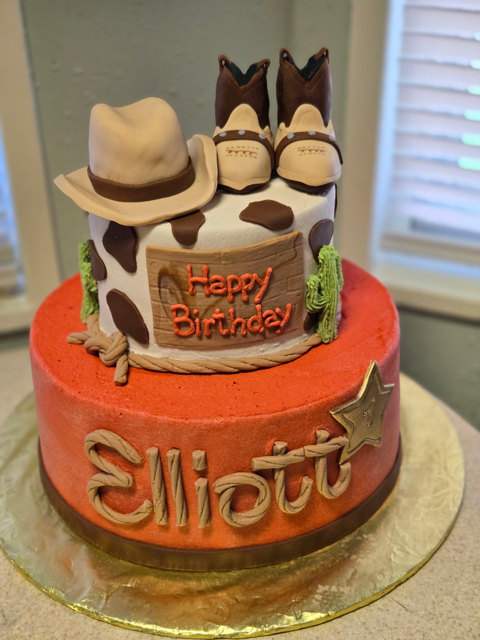 A two-tier rust-colored Western-themed cake with a sculpted cowboy hat and boots
